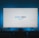 A television screen displays the Prime Video logo, situated on an entertainment unit in a dimly lit room. The room is illuminated with a subtle blue backlight, creating a calming atmosphere. Two small decorative items, resembling mushrooms, are placed on either side of the unit.