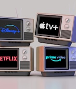 Four old-style television sets are stacked in two rows and each screen displays a different streaming service logo: Disney+, Apple TV+, Netflix, and Prime Video.