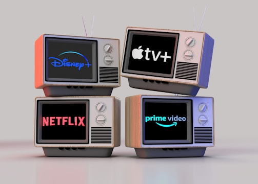 Four old-style television sets are stacked in two rows and each screen displays a different streaming service logo: Disney+, Apple TV+, Netflix, and Prime Video.